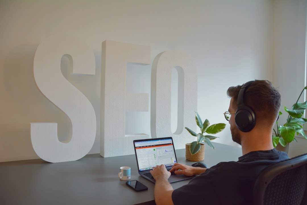Home Focused professional working at an SEO agency, seated at a modern office desk. He is wearing headphones to stay concentrated, with large SEO letters in the background emphasizing the digital environment. On the desk, there is a cup of espresso, a mobile phone, and a small plant, adding a touch of greenery to the workspace.